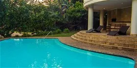 Swimming pool with lounge chairs on a stone patio surrounded by greenery