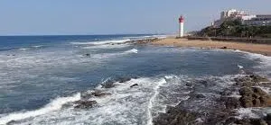 Rocky coastline with waves sandy beach and a lighthouse in the background