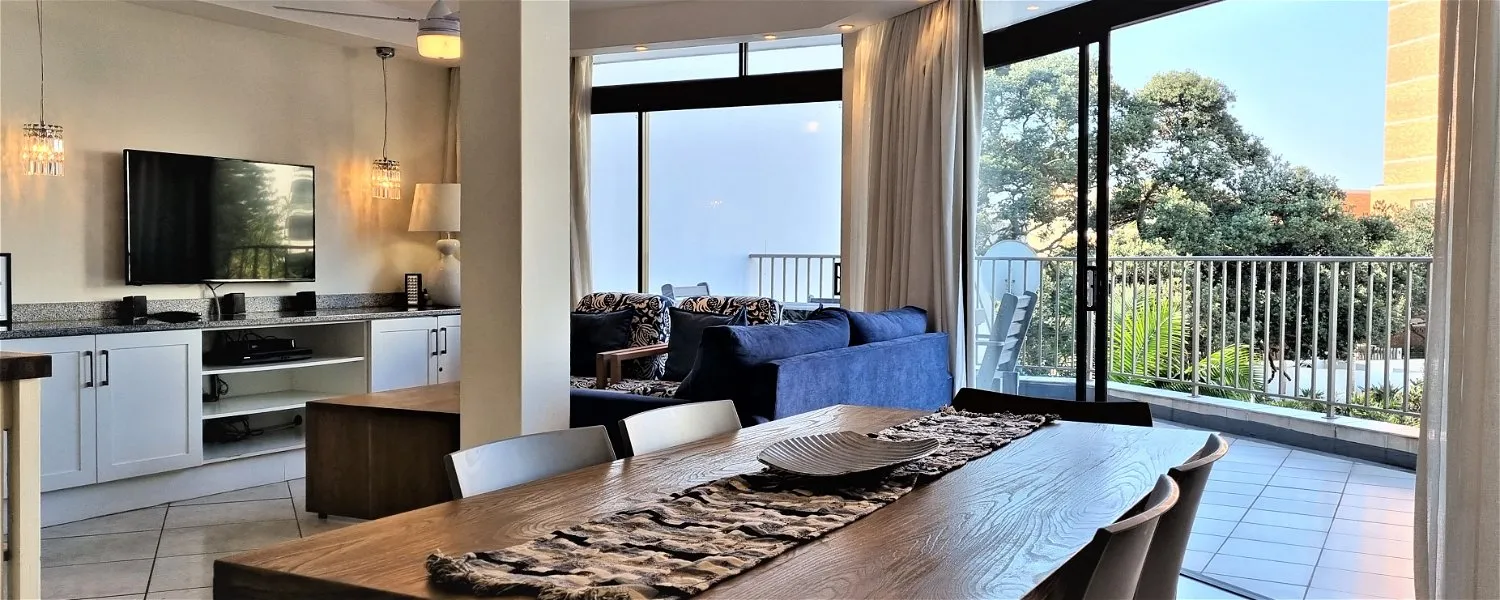 Modern living and dining area with large windows overlooking a balcony and greenery