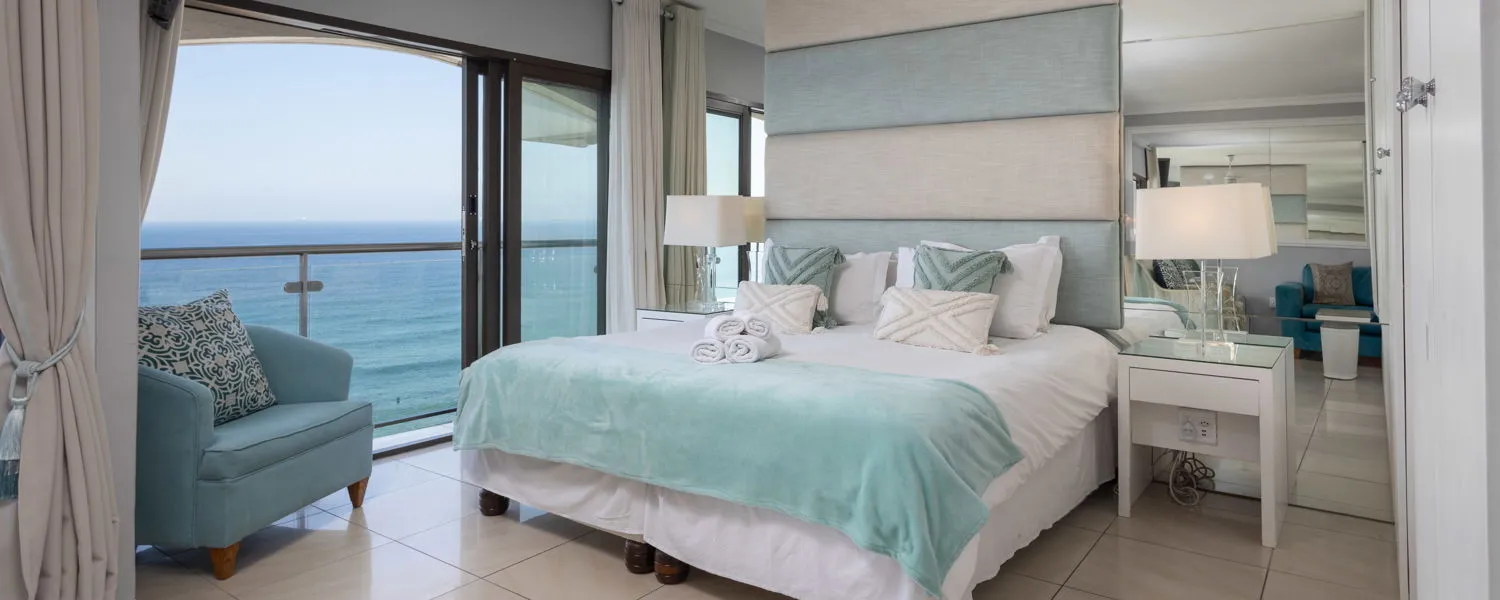 Ocean view bedroom with large bed armchair and sliding glass doors to balcony