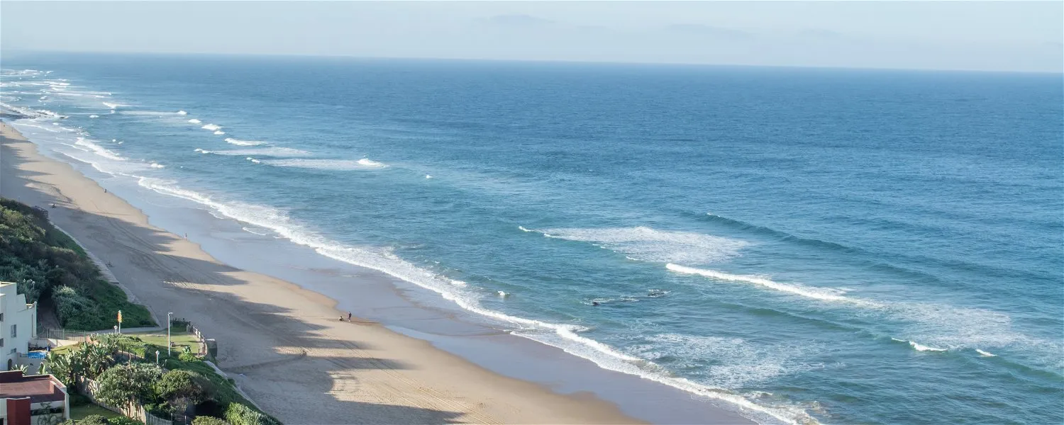 Sandy beach with gentle waves clear blue ocean and buildings on the left