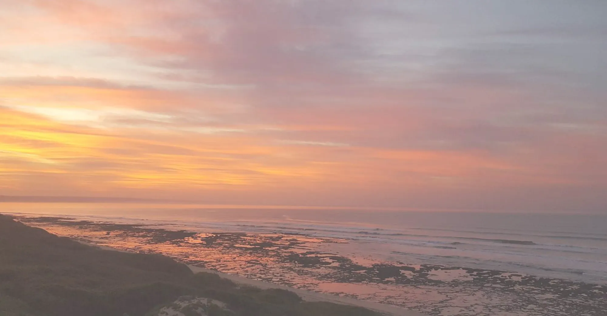 Sunset over a rocky beach with waves gently crashing on the shore