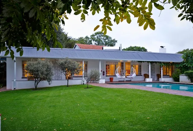 Singlestory house with a pool green lawn and trees in the background