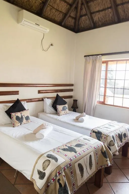 Two single beds with patterned throws in a room with a thatched roof