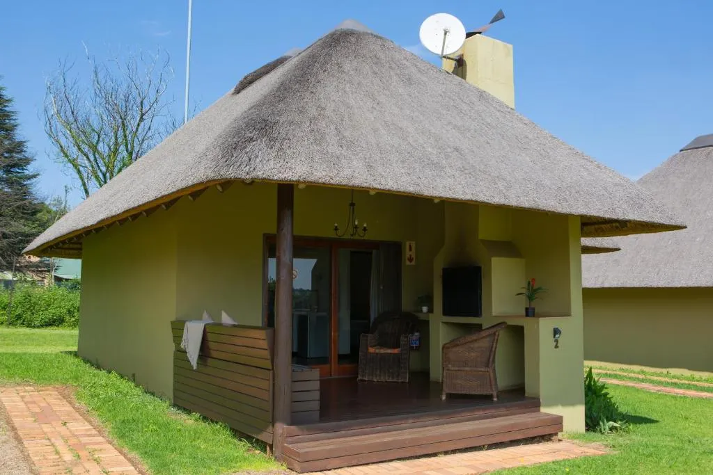 Thatchedroof cottage with a veranda chair and satellite dish on a green lawn