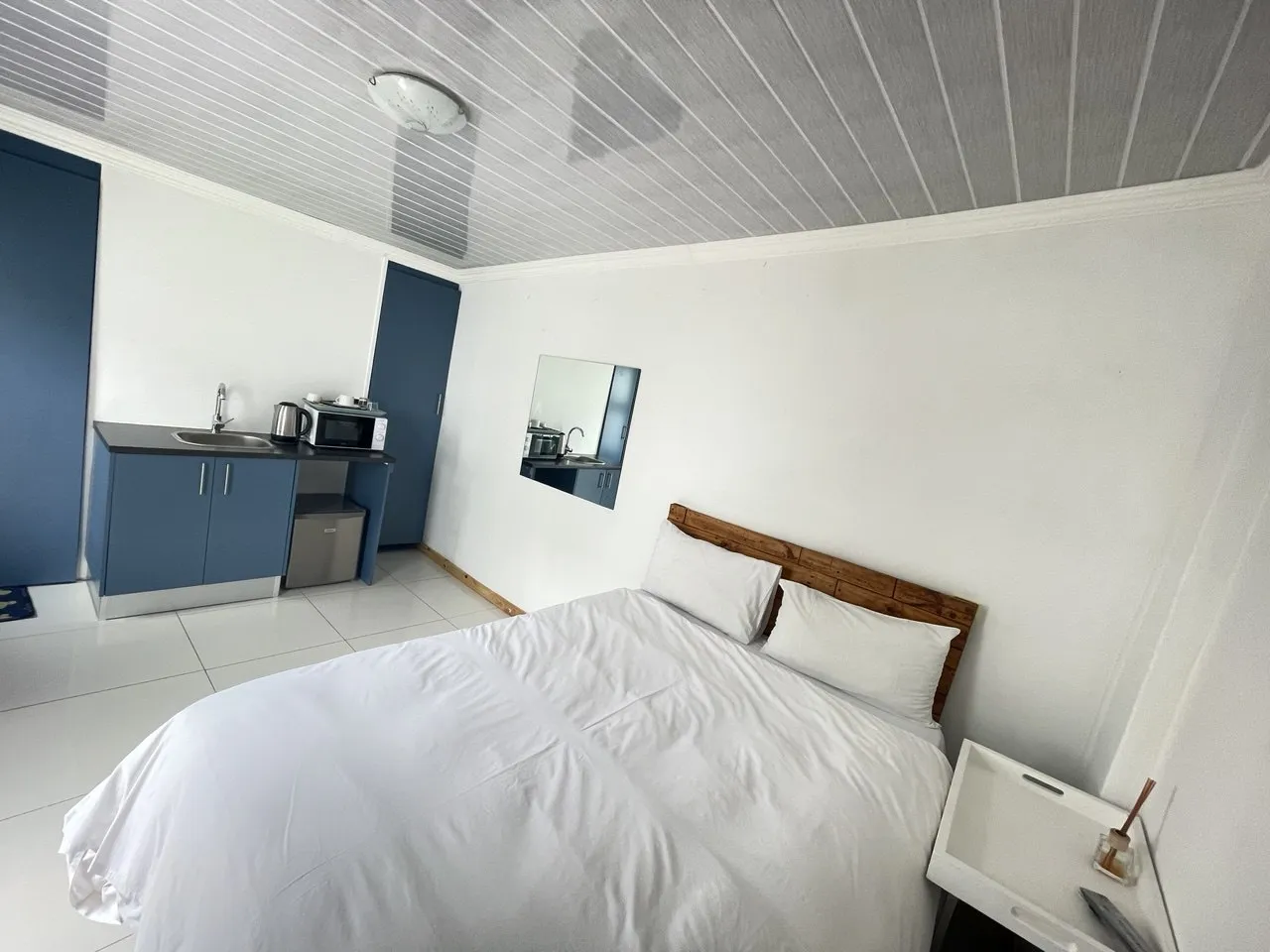 Small bedroom with bed kitchenette and mirror on white walls