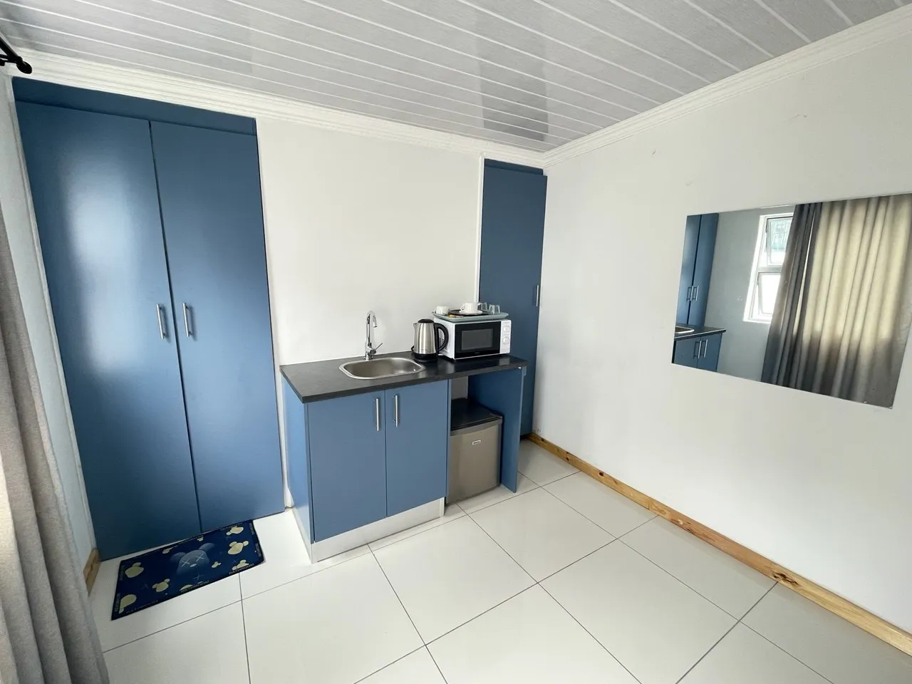 Small kitchen with blue cabinets sink microwave and a mirror on the wall