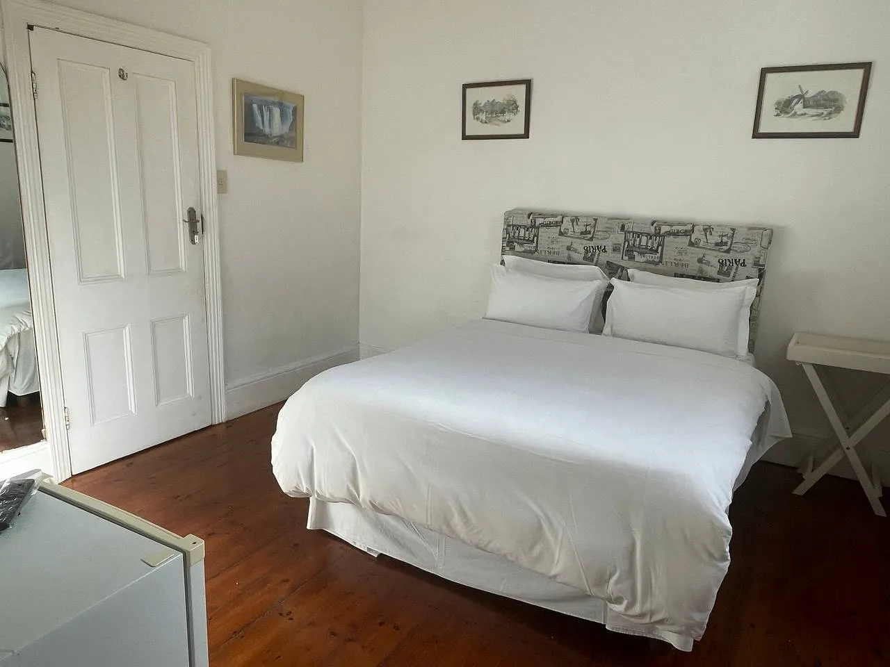 A neatly made bed in a simple bright bedroom with wooden floor