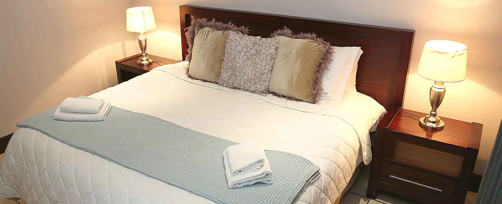A neatly made bed with pillows towels and bedside lamps in a bedroom