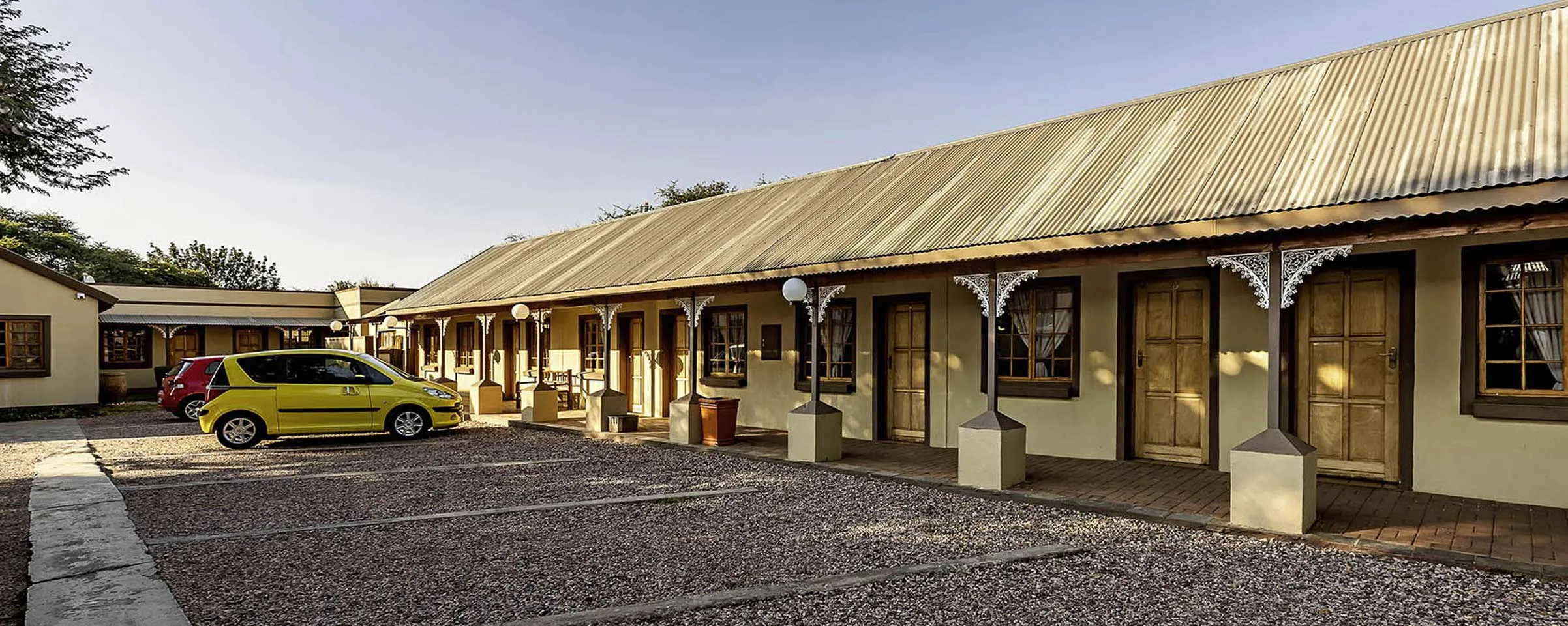 Row of singlestory buildings with yellow car parked in front gravel lot