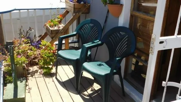 Two green chairs on a wooden deck with flowers and a railing