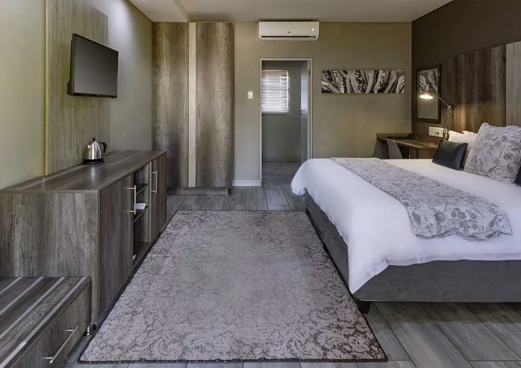 Modern hotel room with bed TV desk and wooden furniture on tiled floor