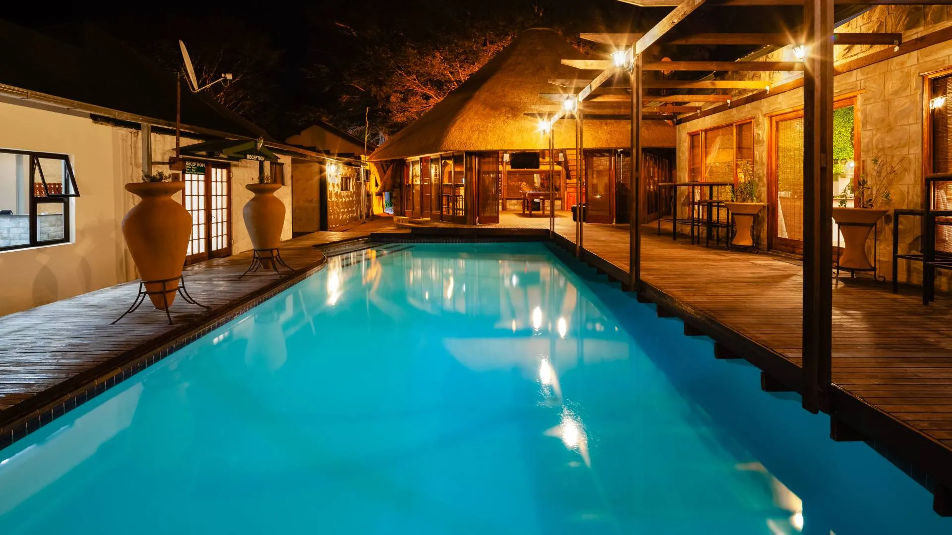Night view of a lit poolside area with wooden deck and rustic buildings