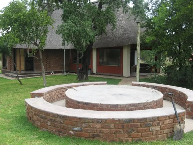Circular brick bench around a concrete platform in front of a thatchedroof building