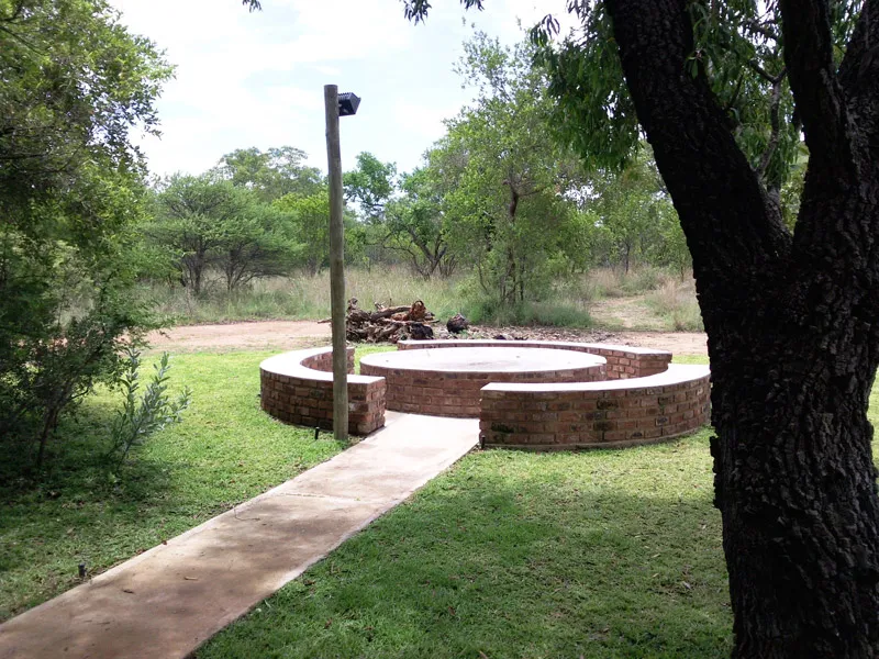 Circular brick fire pit in a grassy area with trees and a pathway