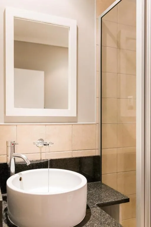 Modern bathroom with white sink black countertop mirror and beige tiled wall