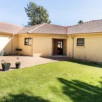 Singlestory house with tiled roof green lawn and potted plants in front