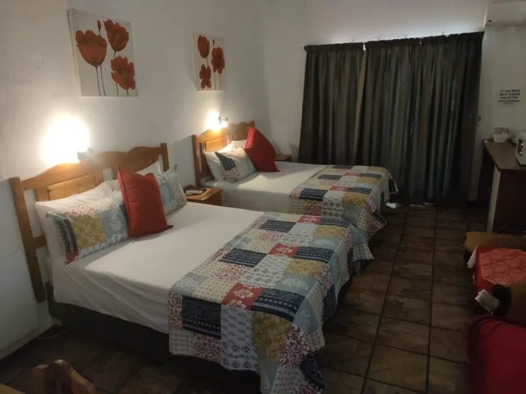 Two twin beds with colorful quilts in a bedroom with tiled floor and curtains