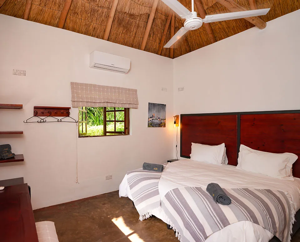 Cozy bedroom with two beds thatched ceiling and a small window