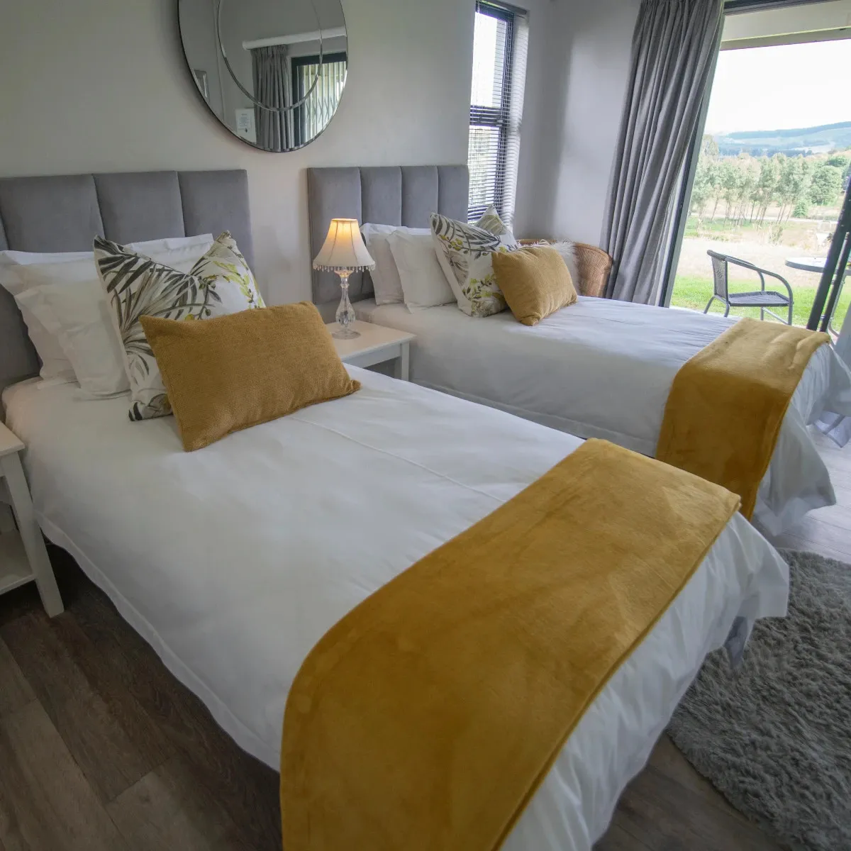 Two beds with yellow throws in a bright modern bedroom with a garden view