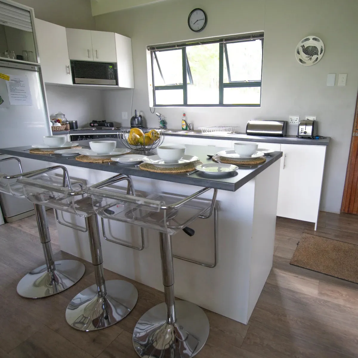Modern kitchen with island stools and dining setup near window and clock