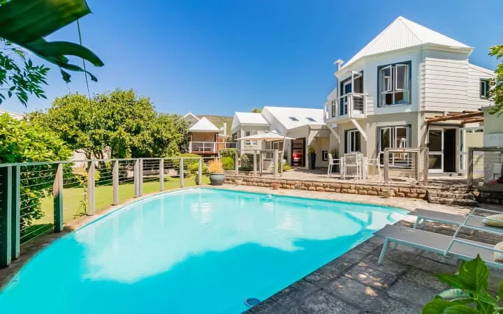 Modern house with swimming pool lounge chairs and lush greenery in sunny weather