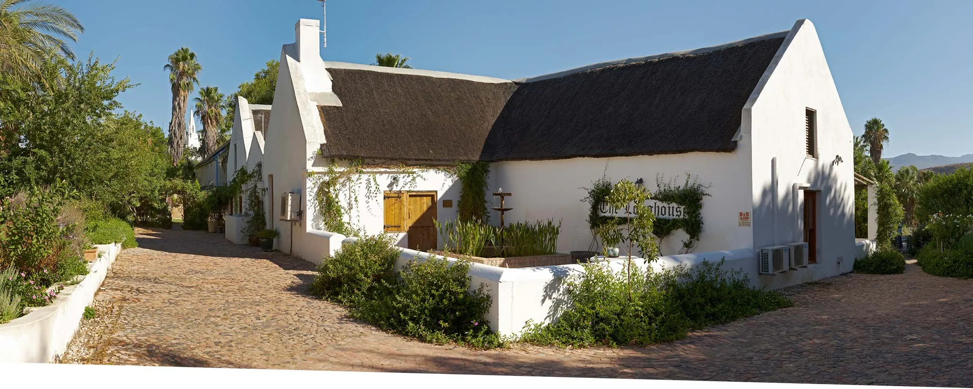White cottage with thatched roof surrounded by greenery and palm trees