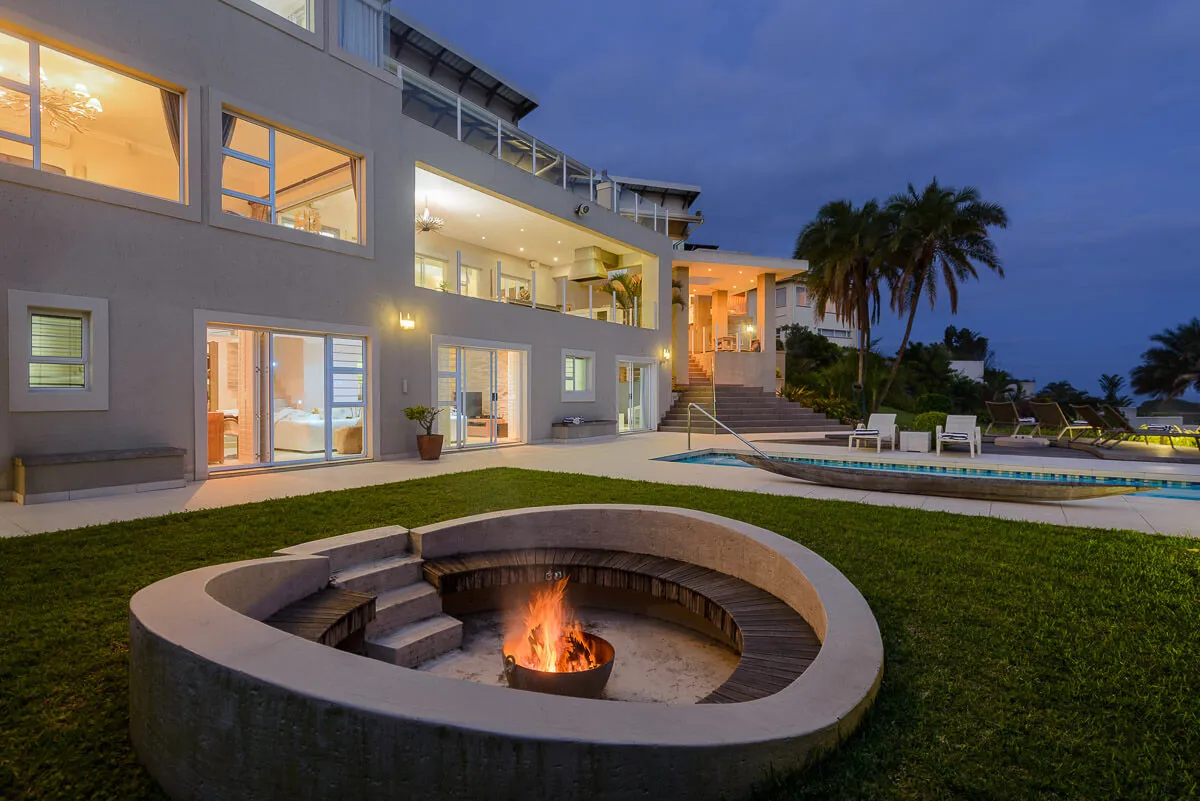 Modern house at night with lit fire pit in the foreground and pool