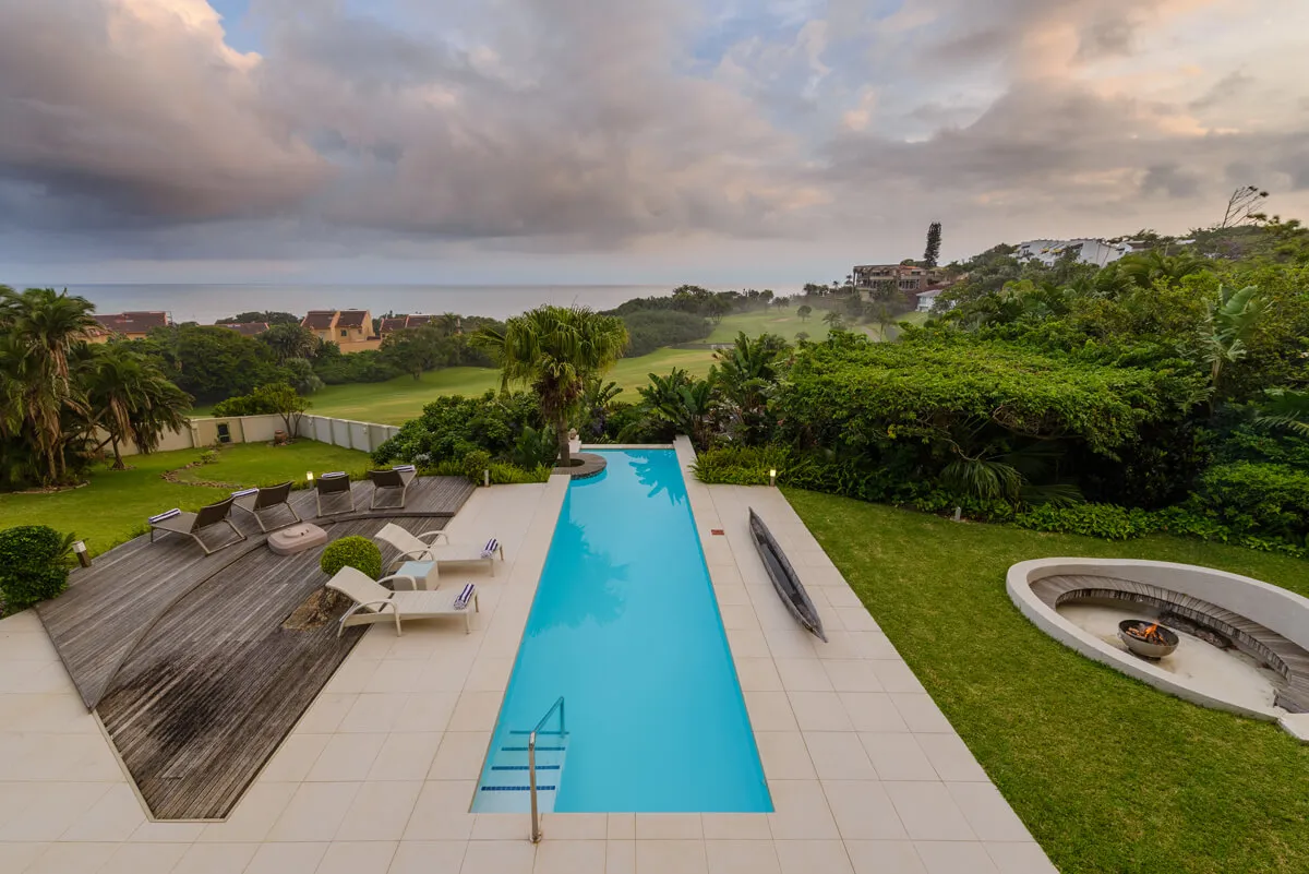 Modern pool with lounge area overlooking a scenic landscape with greenery and ocean