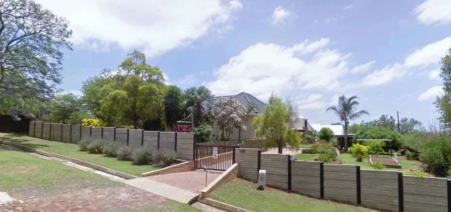 House with garden fenced yard and driveway under a blue sky with clouds