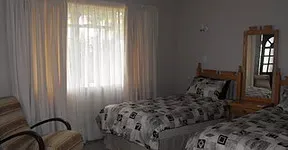 Bedroom with two single beds patterned bedding armchair and window with sheer curtains