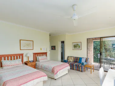 Bedroom with two single beds sofa ceiling fan and sliding door to balcony