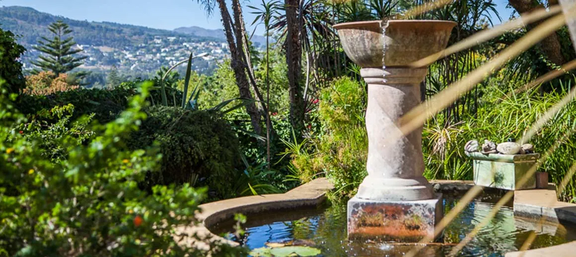 Stone fountain in a lush garden with a scenic hillside view