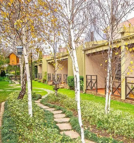 Pathway through a garden with trees and small buildings in the background