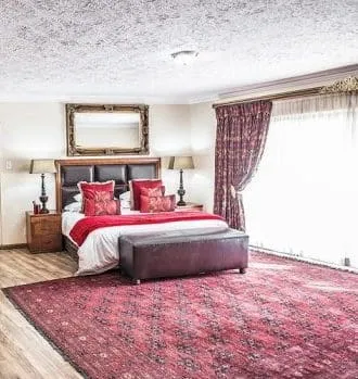 Bedroom with large bed red decor and large window with curtains