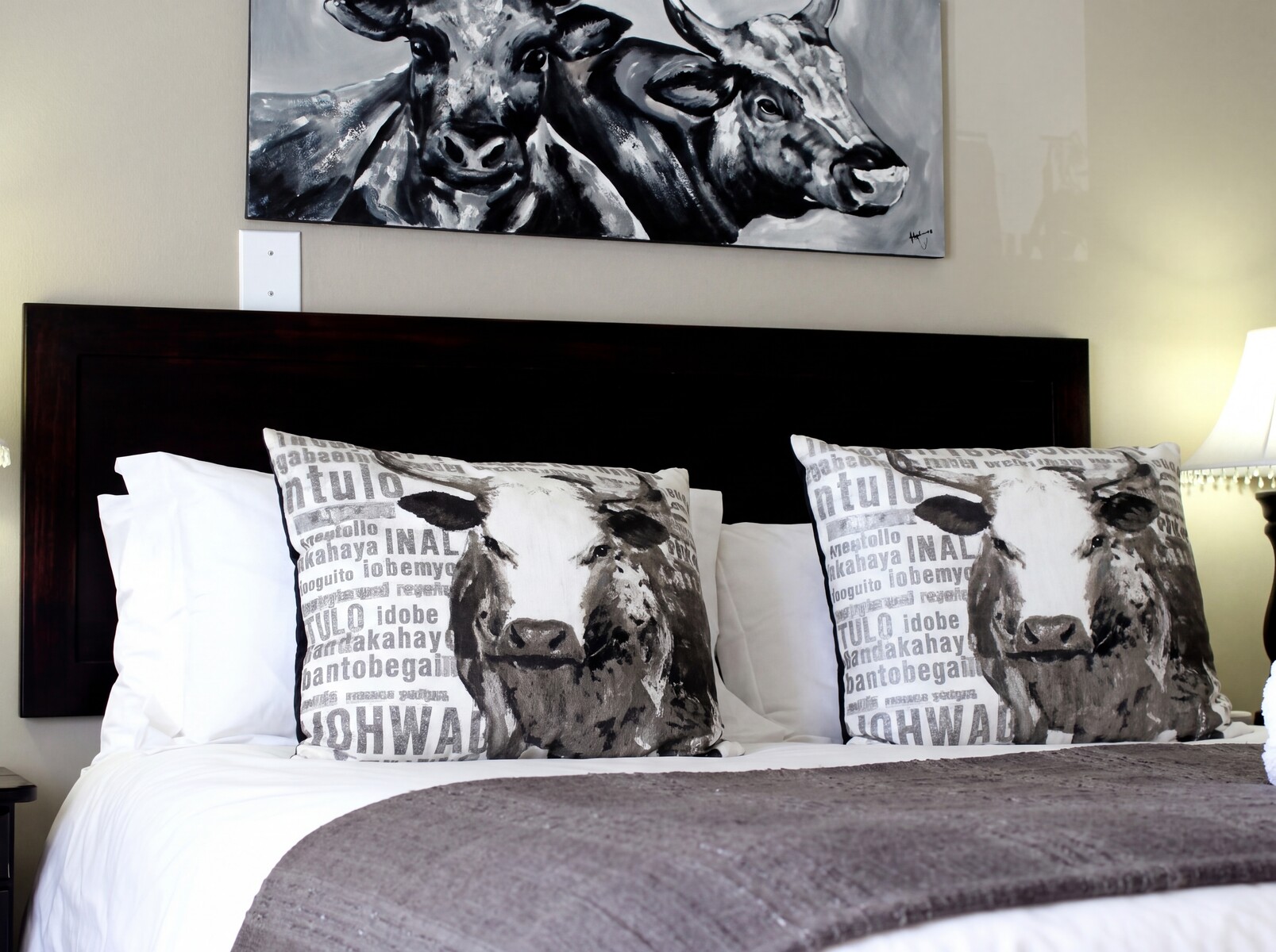 Bedroom with a bed cowthemed pillows and a matching wall art piece