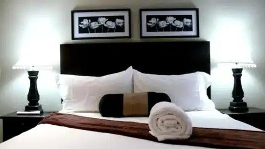Neatly made bed with white linens black headboard and bedside lamps