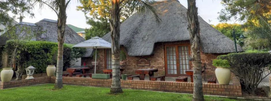 Thatchedroof building with outdoor seating and palm trees in a garden setting