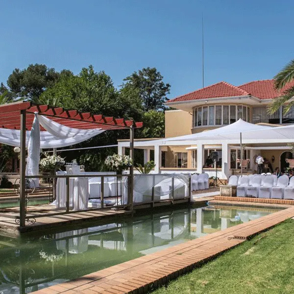 Outdoor wedding setup with white chairs tables and a pool in front of a house