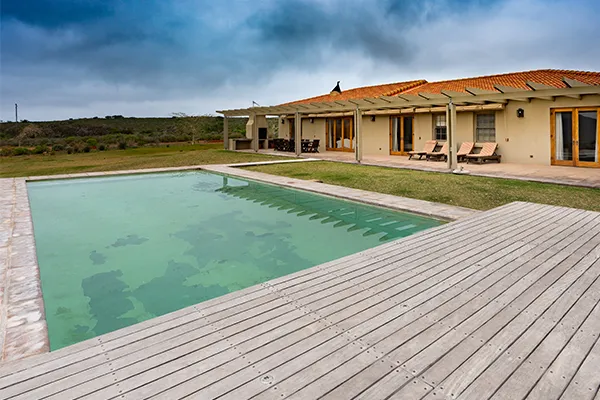 Swimming pool with wooden deck in front of a house with a tiled roof