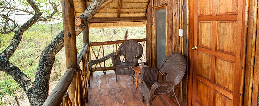 Wooden balcony with wicker chairs overlooking trees rustic cabin door