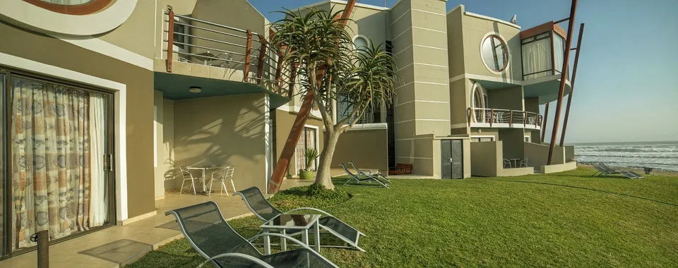 Modern beachfront house with lounge chairs on a grassy lawn near the ocean
