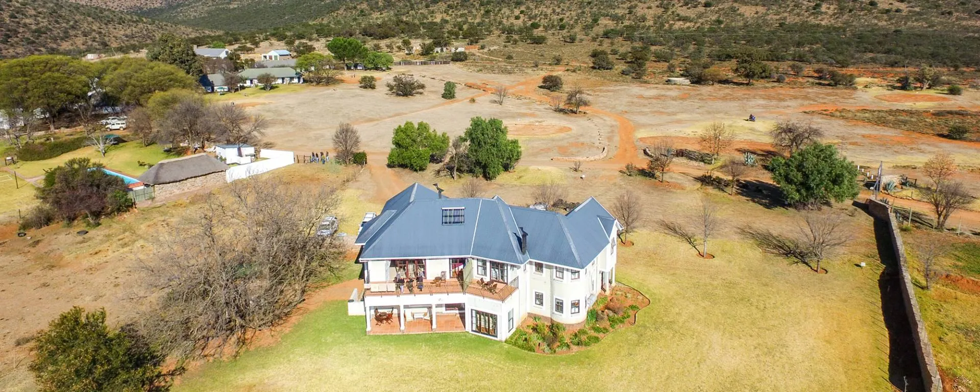 Large house with blue roof in a rural open landscape with scattered trees