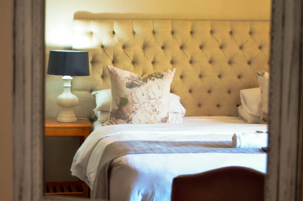 A neatly made bed with pillows in a bedroom with a bedside lamp
