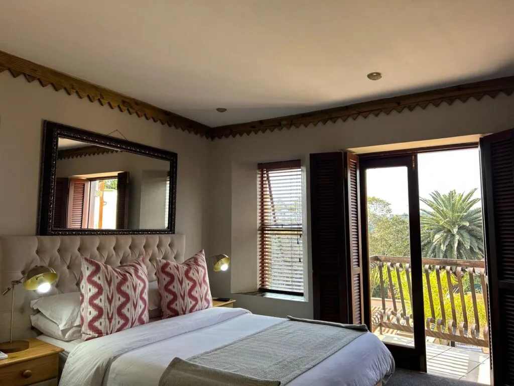 Bright bedroom with large mirror patterned pillows and open balcony doors to garden