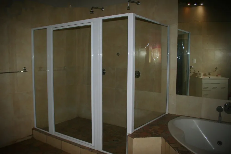 Modern shower with glass doors in a tiled bathroom with a bathtub and mirror