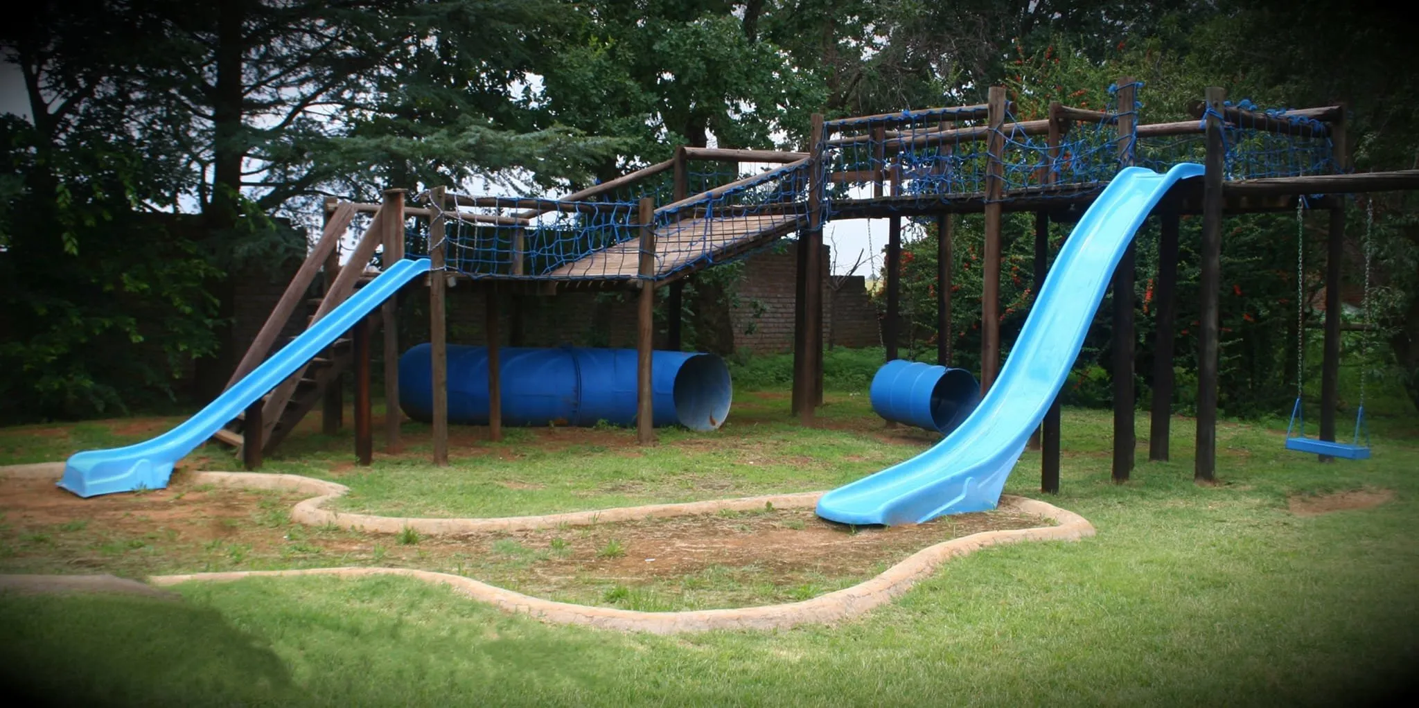 Playground with slides tunnels and swings surrounded by grass and trees