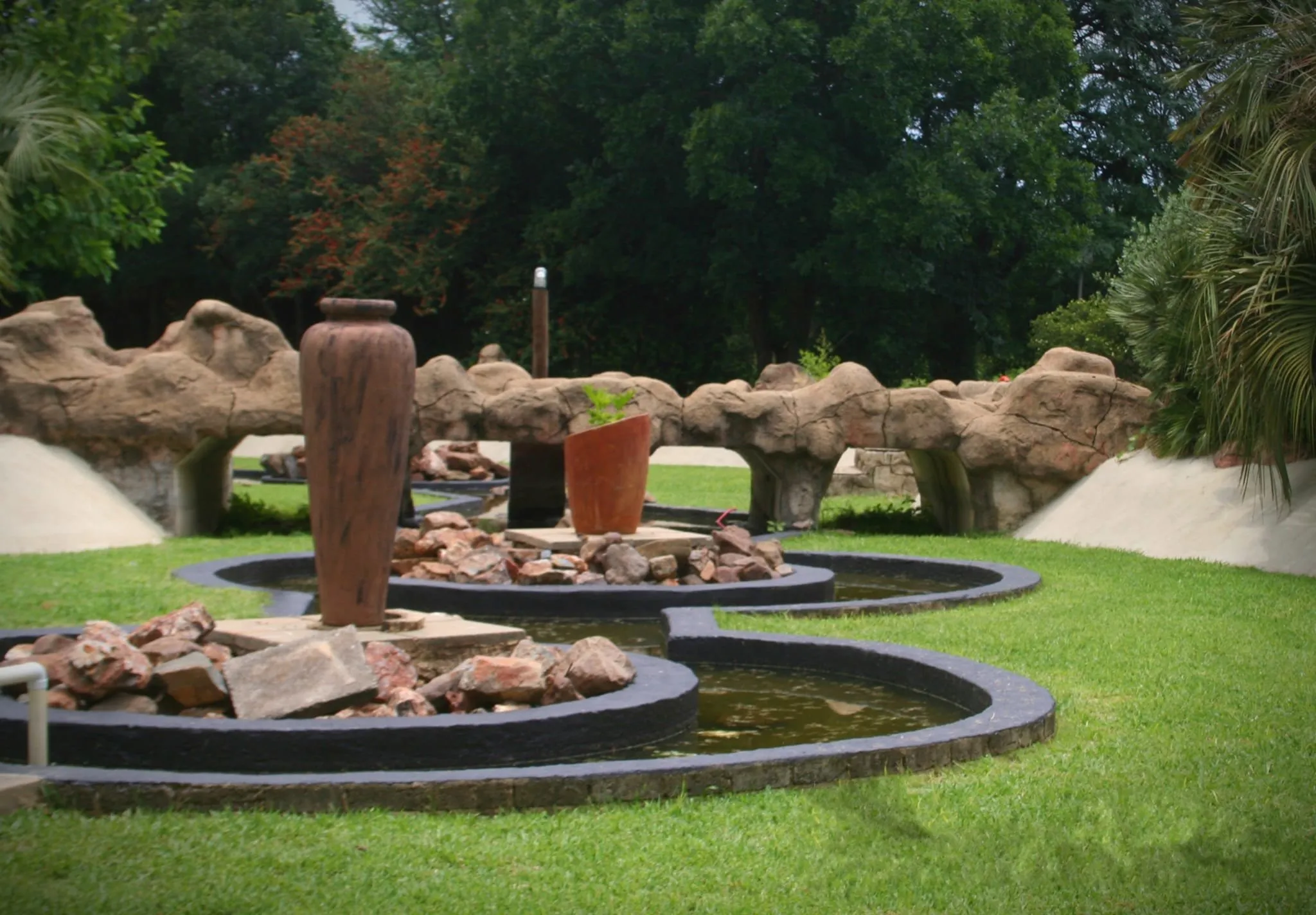 Garden with stone sculptures large vases and a pond surrounded by greenery