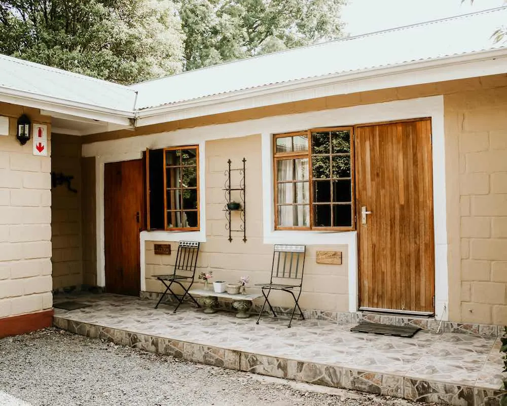 Wooden door and windows of a beige house with chairs on a stone patio