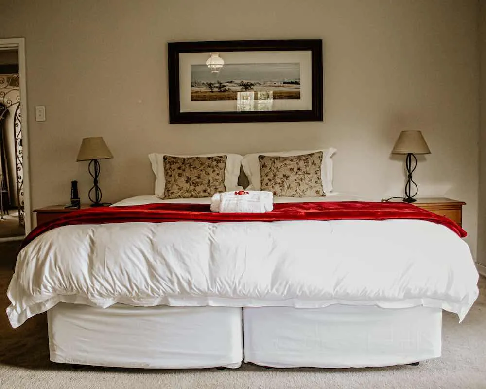 Bedroom with large bed white comforter red throw and bedside lamps